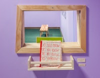 a purple wall with a mirror and a book on a shelf